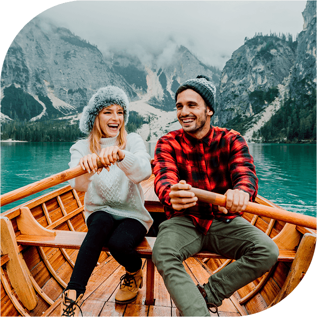 A man in a woman sit in a rowing boat, rowing along a river between some mountains